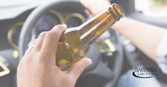 Image of a man holding a beer in his left hand and his right hand on the steering wheel.